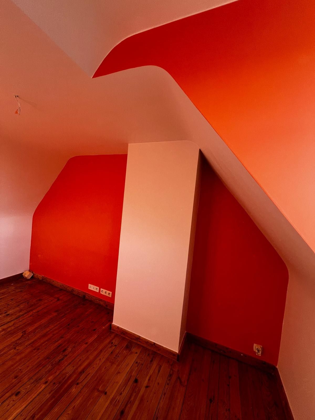 Chambre sous pente entièrement repeinte en rouge vif, parquet ancien au sol