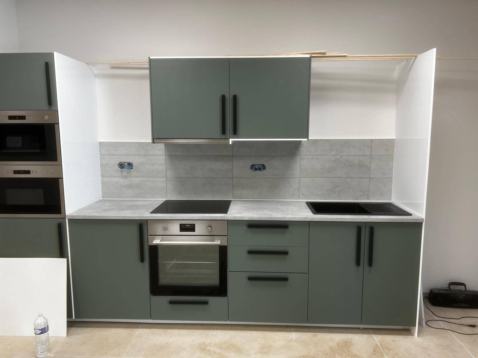 Cuisine équipée aux façades vert olive avec four, plaque et hotte, sur un sol carrelé clair