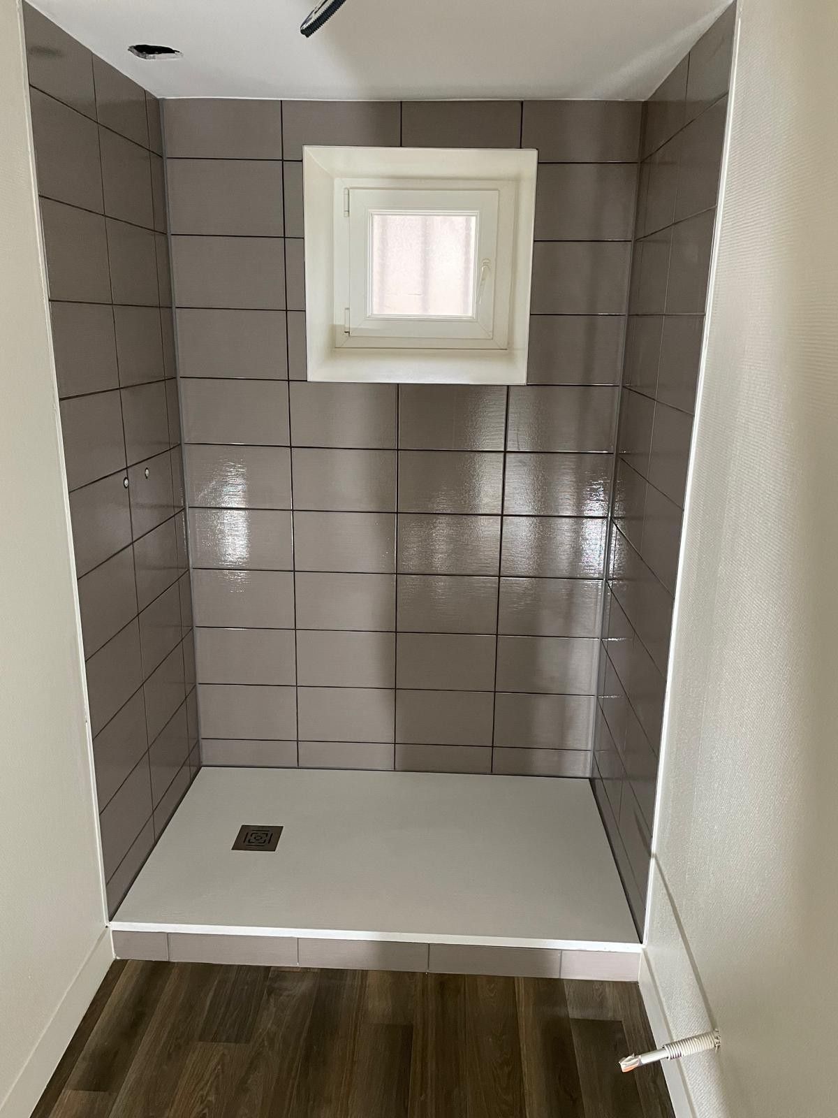 Douche carrelée en grandes dalles grises avec receveur extra-plat et fenêtre