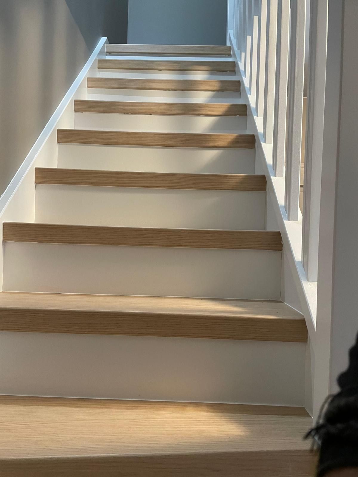 Escalier droit vu depuis le bas, marches en bois clair et garde-corps blanc