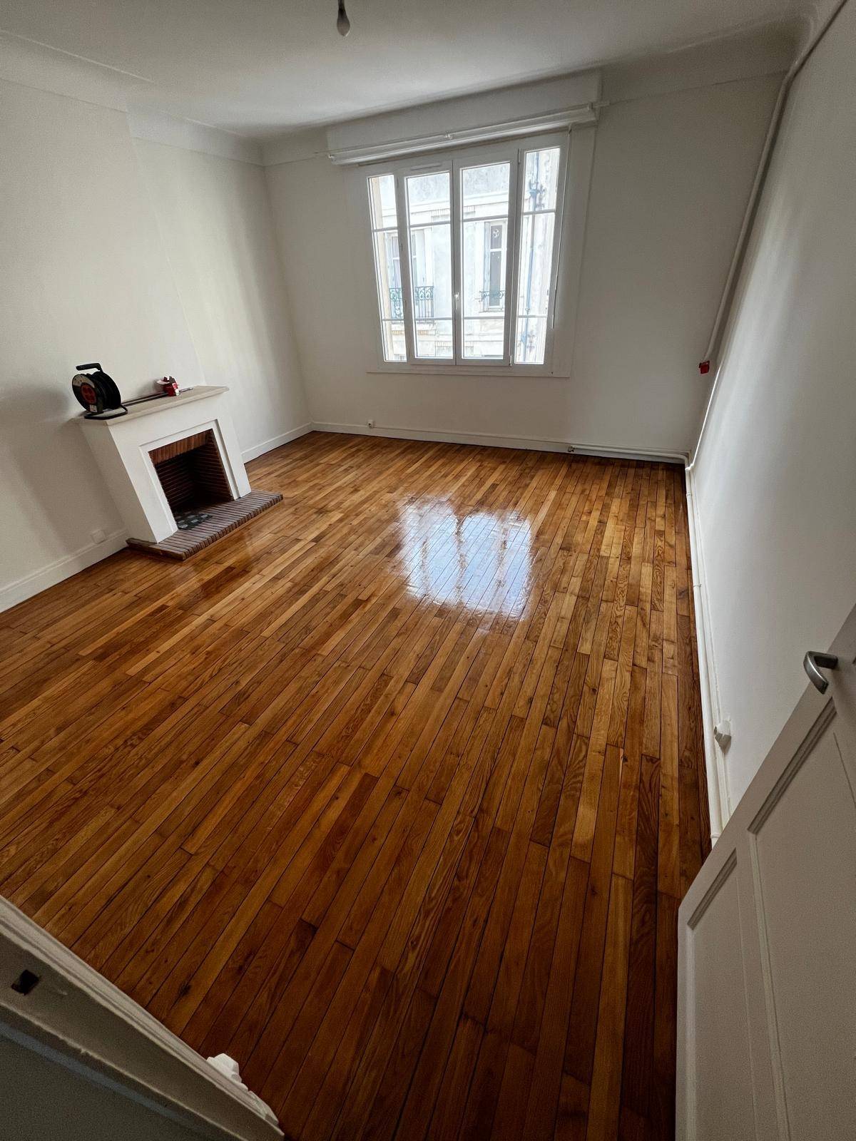 Pièce vide au parquet en bois massif fraîchement verni, avec une cheminée et une fenêtre