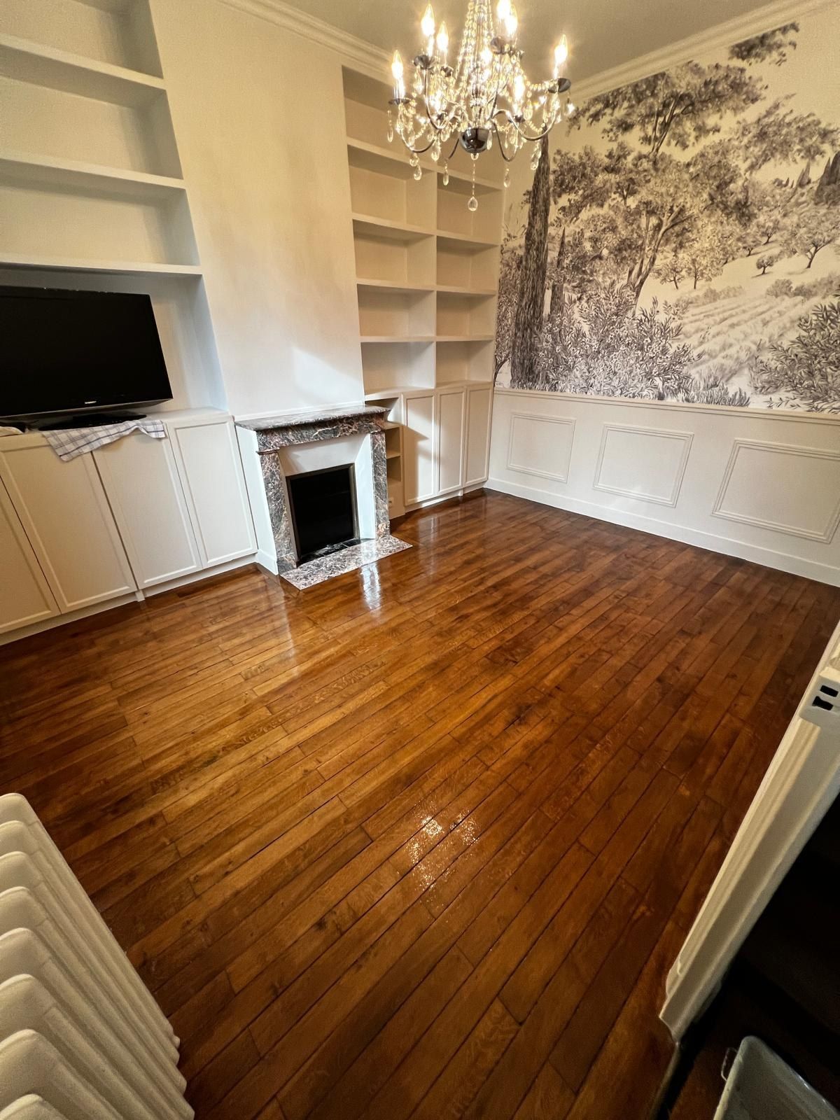 Salon avec un décor mural panoramique au-dessus de la cheminée, boiseries blanches et parquet