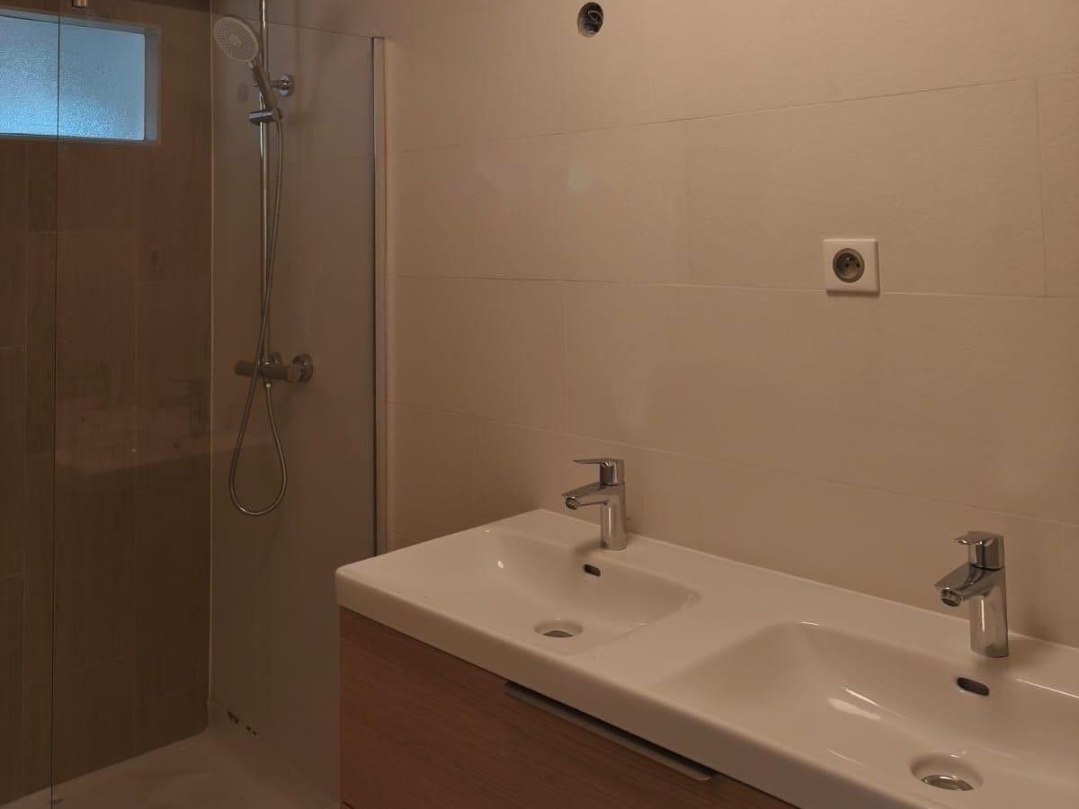 Après travaux : la même salle de bain avec une douche vitrée, un carrelage beige et un meuble double vasque