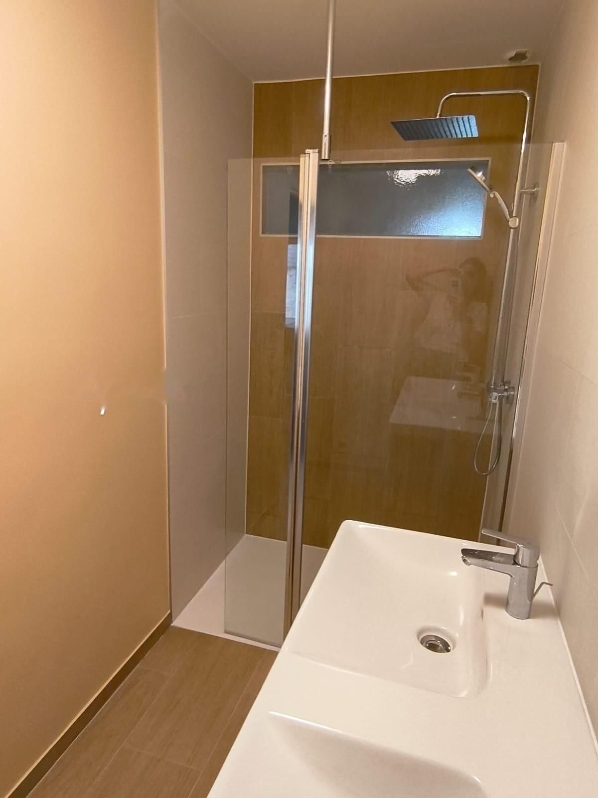 Salle de bain avec douche à l’italienne vitrée, plan vasque blanc et carrelage aspect bois