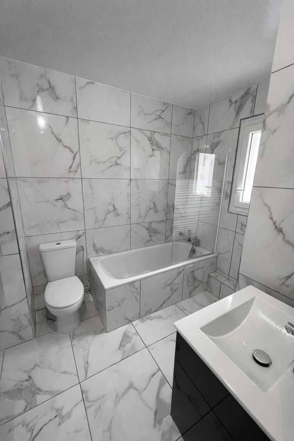 Salle de bain carrelée effet marbre avec baignoire, WC et plan vasque