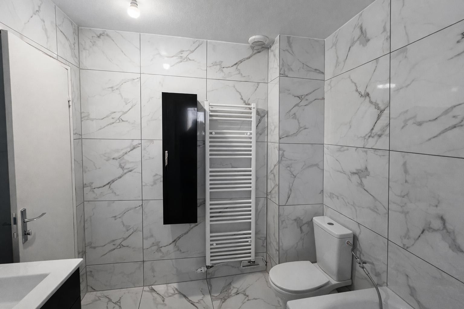 Salle d’eau carrelée effet marbre du sol au plafond, avec sèche-serviettes noir et WC suspendu