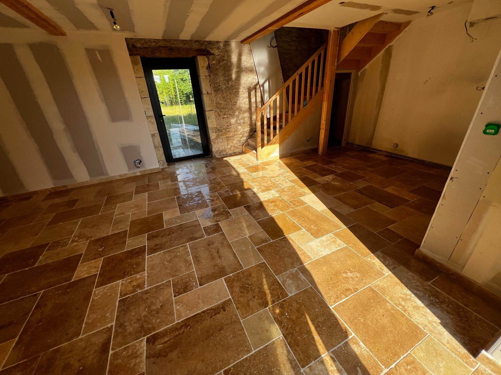 Pose d’un sol en travertin en opus dans une maison en rénovation, près d’un mur en pierre et d’un escalier en bois