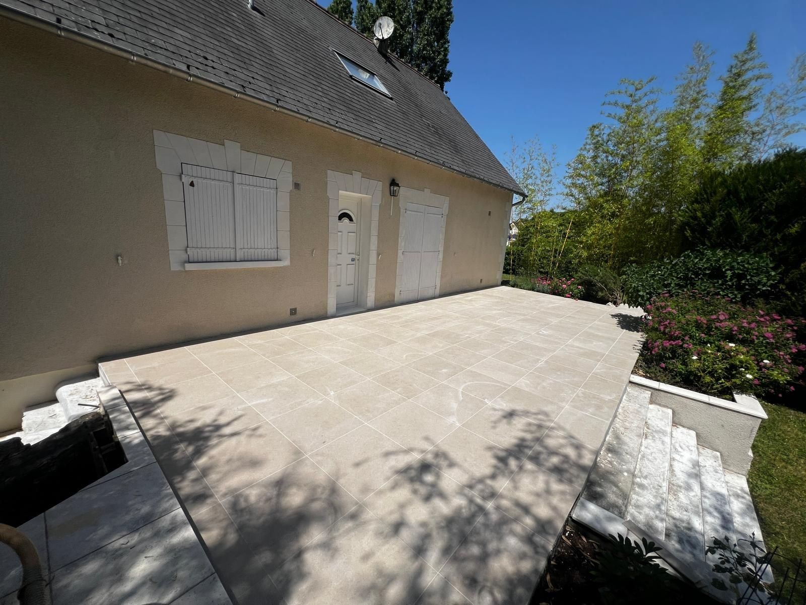 Terrasse carrelée en dalles claires le long de la façade d’une maison en tuffeau